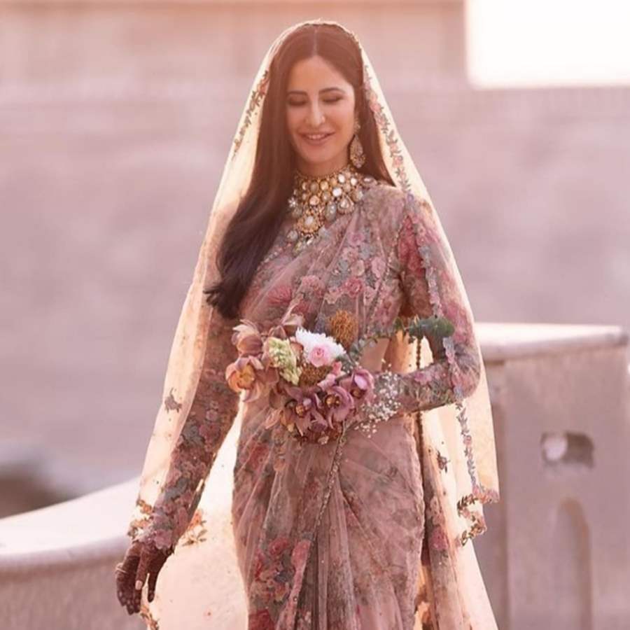 a beautiful woman wearing traditional Indian garb, possibly a saree, with a  green and gold border. She is sitting down and wearing a yellow veil, which  adds a pop of color to