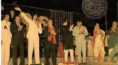 The nostalgic picture captures Amitabh Bachchan waving while holding a microphone on stage, surrounded by luminaries such as Vinod Khanna, Raj Kapoor, Rekha, Shammi Kapoor, Randhir Kapoor, Mehmood, and music director Kalyan.