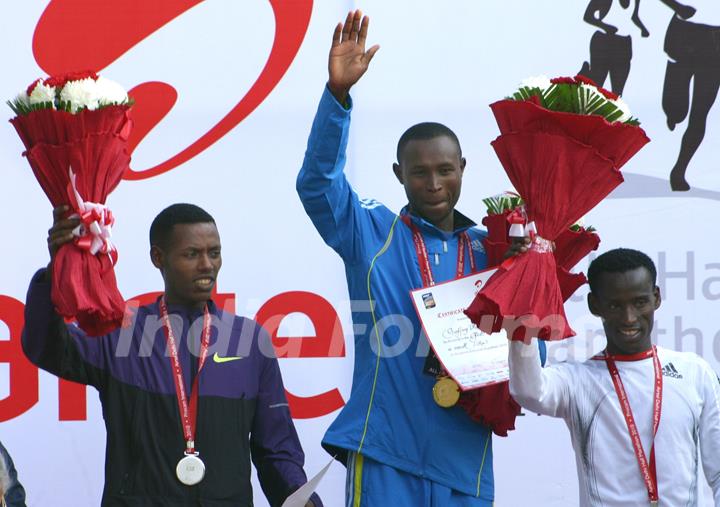 Geoffrey Mutai (R) of Kenya waves after winning gold in the men's  event of Delhi half Marathon, along with silver medallist Lelisa Desisa (L) of Ethiopia and bronze medal winner Yacob Yarso of Ethopia during the victory ceremony , in New Delhi